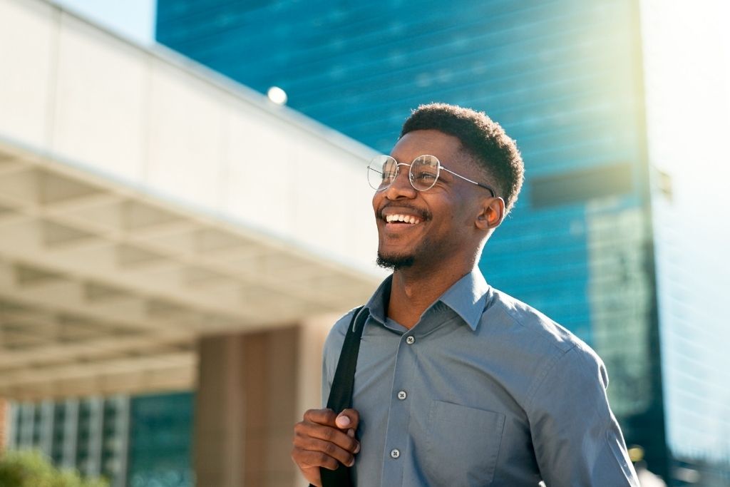 Profissional sorridente caminhando em ambiente corporativo moderno, representando employee experience positiva ligada a bem-estar, autonomia e rotina de trabalho equilibrada.