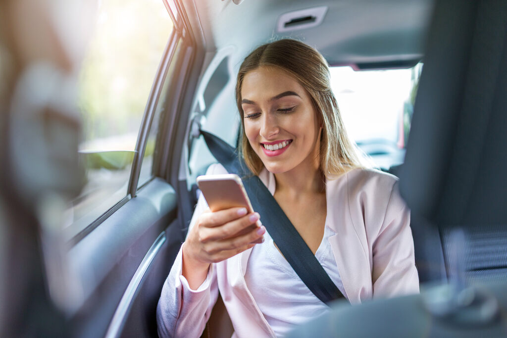 Mulher sorridente em carro de aplicativo de transporte, representando a flexibilidade do formato de vale transporte.
