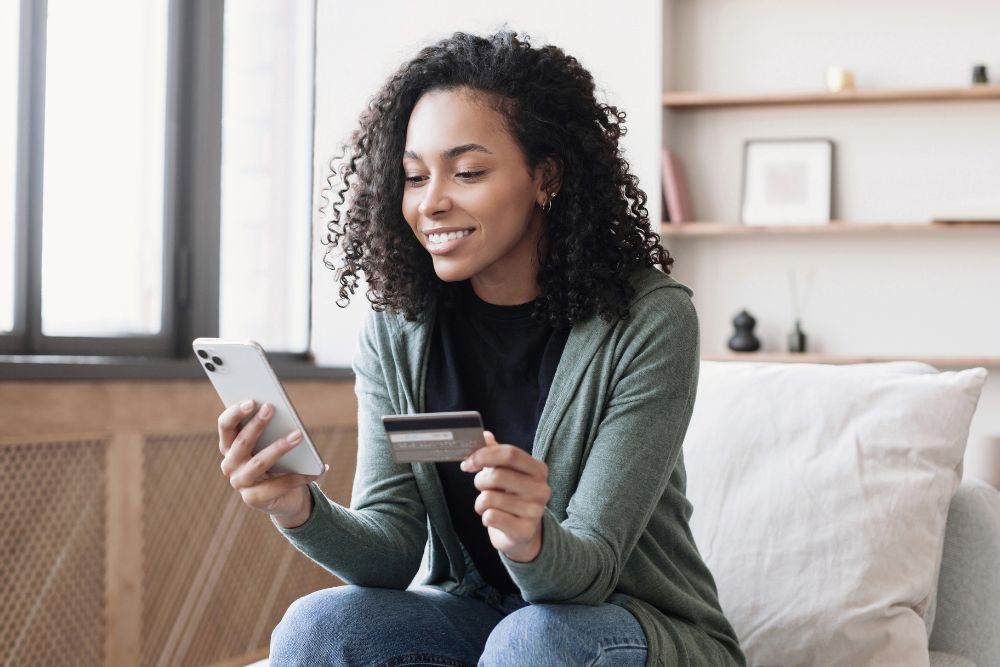 Profissional consulta informações de seu cartão multibenefícios físico enquanto utiliza um smartphone em sua estação de trabalho.