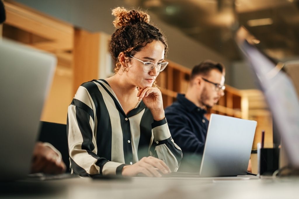 Profissional de RH em um ambiente de escritório, focada no trabalho, utilizando um laptop. Ela está analisando dados e processos, refletindo sobre como a redução de custos pode ser aplicada na gestão de benefícios corporativos através da tecnologia.