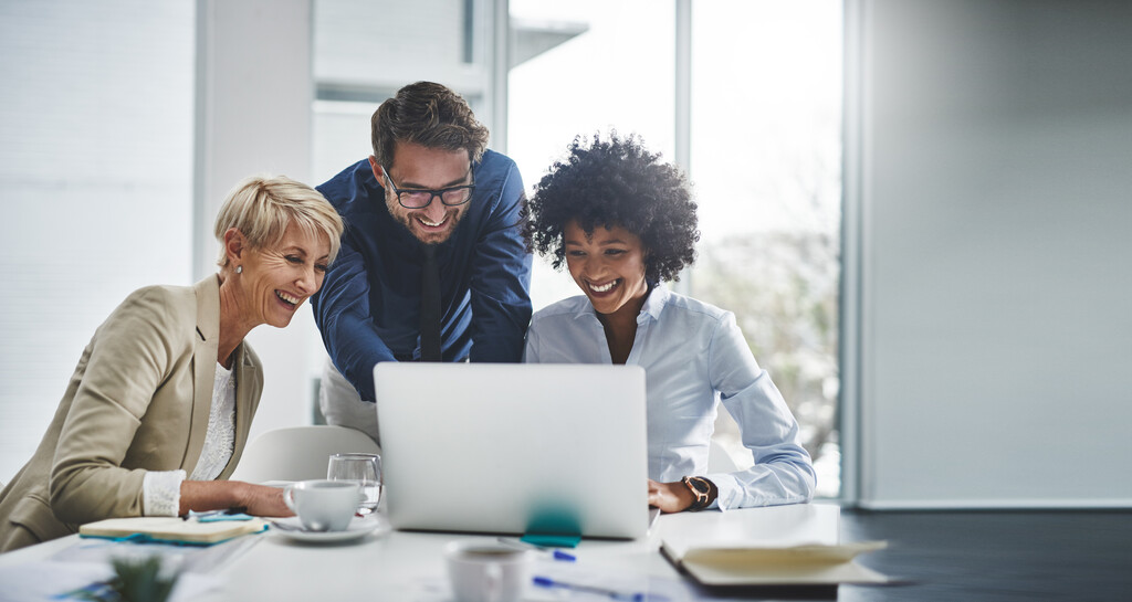 Três colaboradores em escritório, sorridentes ao conferirem impactos dos benefícios supletivos.