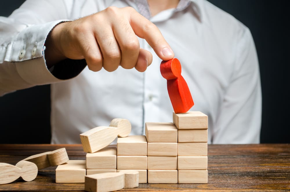 Mão de profissional remove figura de pessoa de um conjunto organizado, representando o conceito de turnover e a saída de colaboradores no ambiente corporativo.