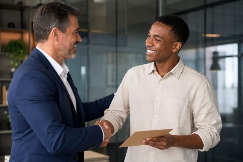 Gestor aperta a mão de um colaborador sorridente em um ambiente corporativo moderno, simbolizando o reconhecimento pelo prêmio de assiduidade e a valorização do comprometimento profissional.